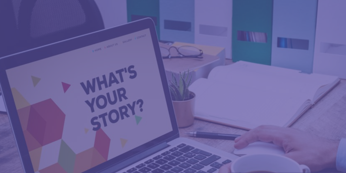 Pessoa com um computador portátil aberto que exibe a mensagem “What’s your story?”, sobre uma secretária com caderno, chávena, óculos e pastas de arquivo ao fundo.